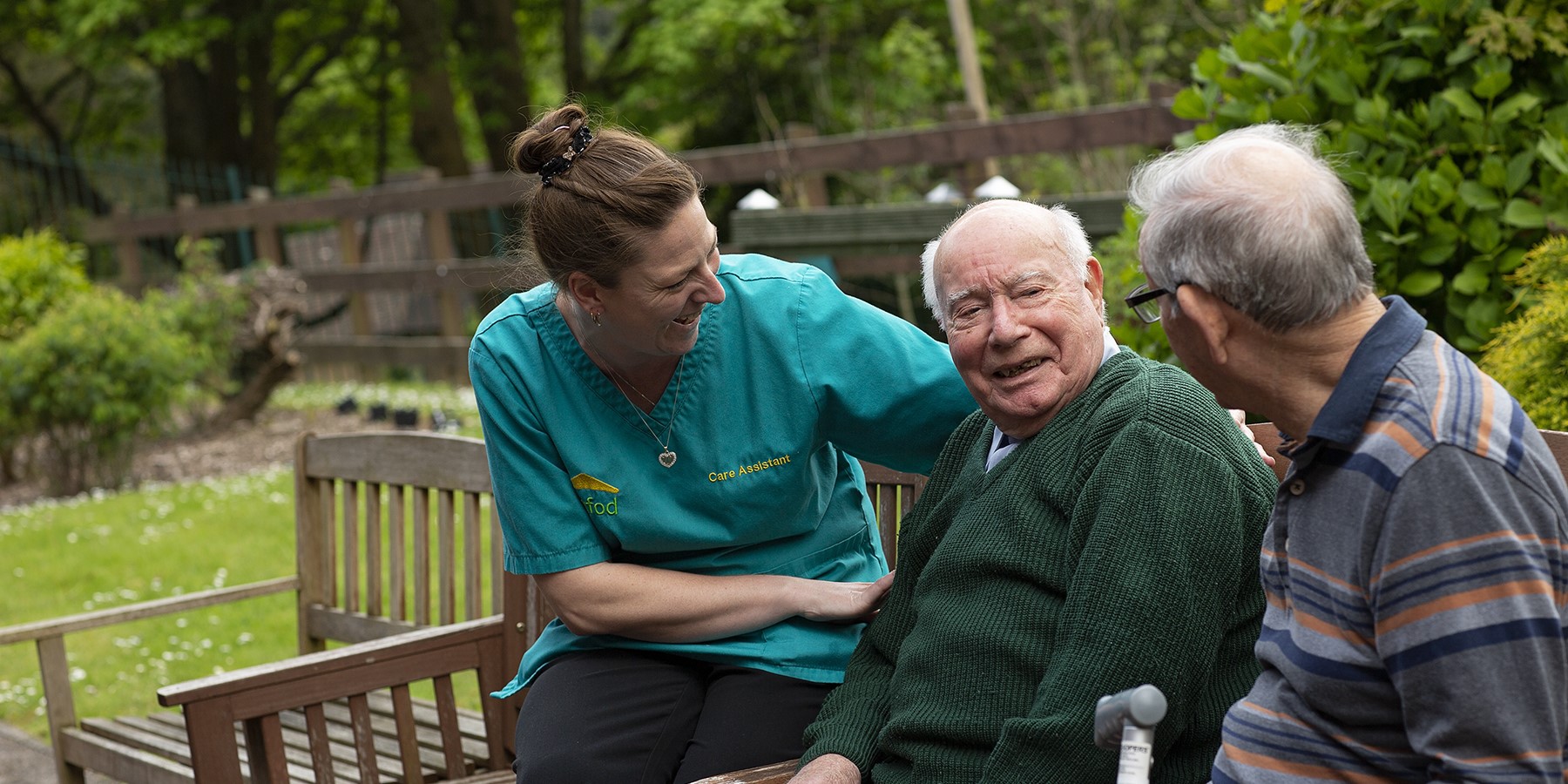 Carer talking to two residents on wooden bench in the garden