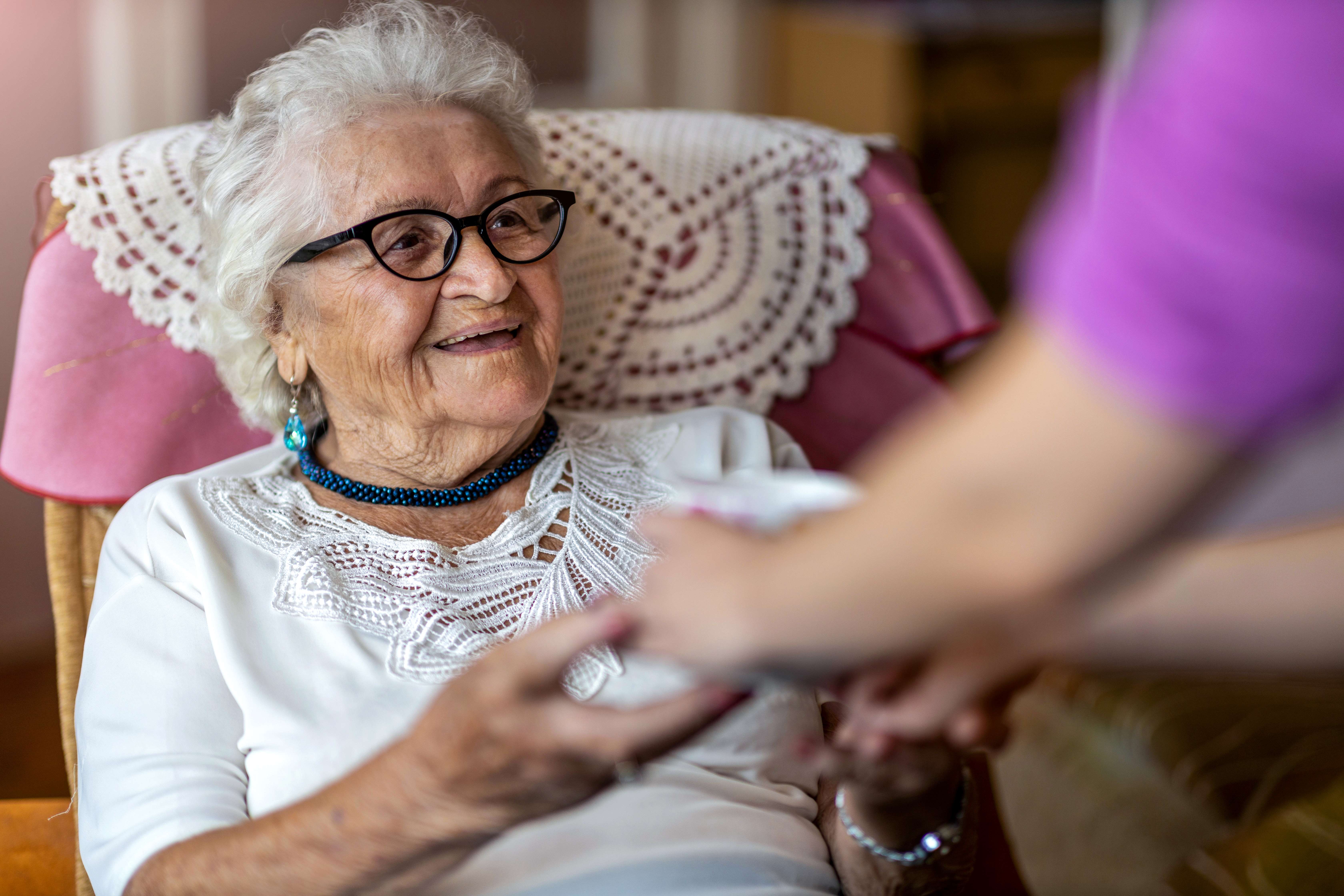 Lady holding hands with her carer while sitting in an armchair