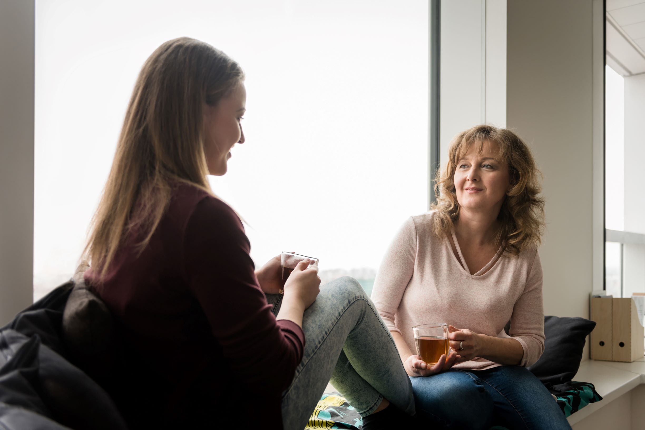 Two ladies chatting and drinking tea on a window seat