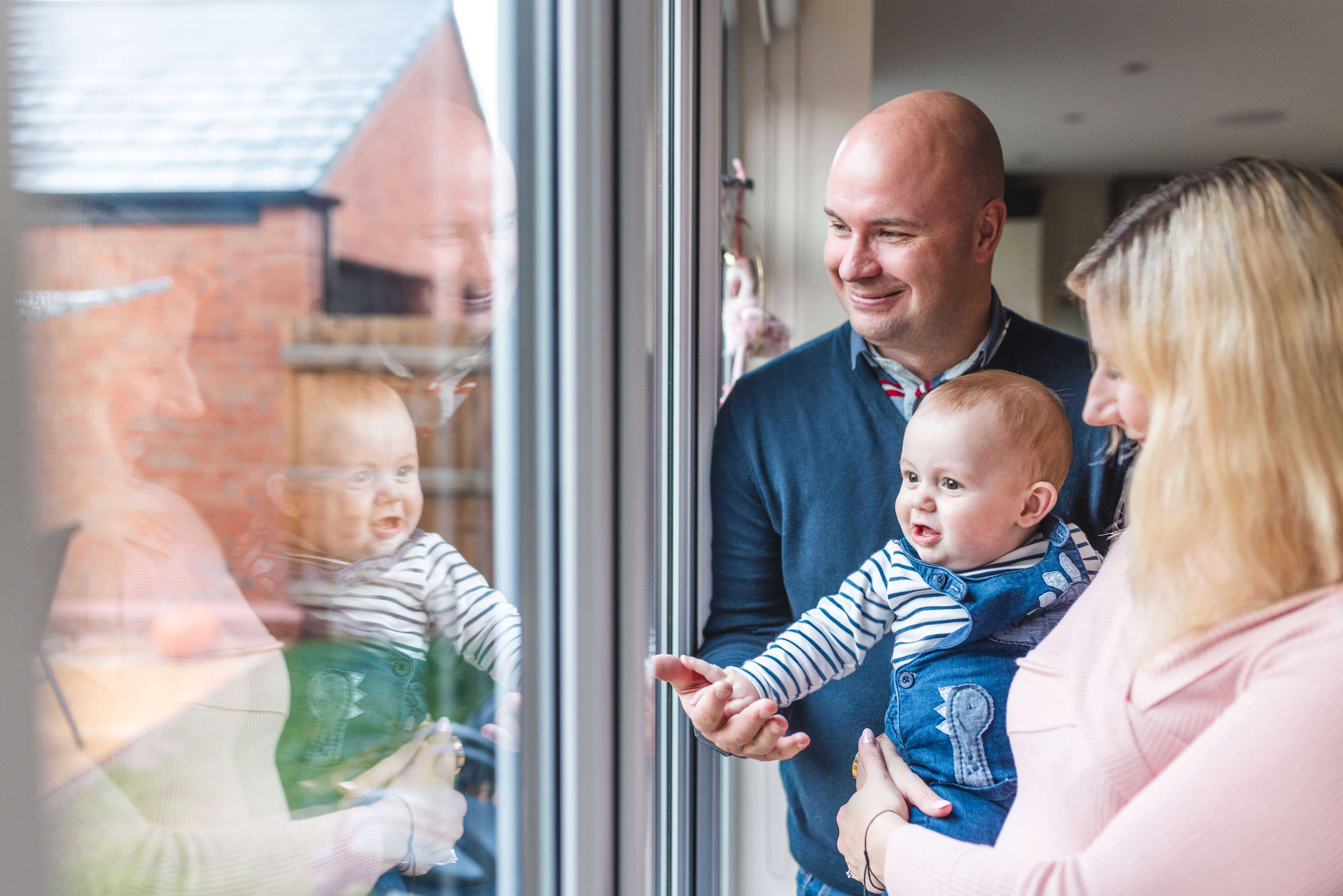Couple holding their baby and looking out their patio doors