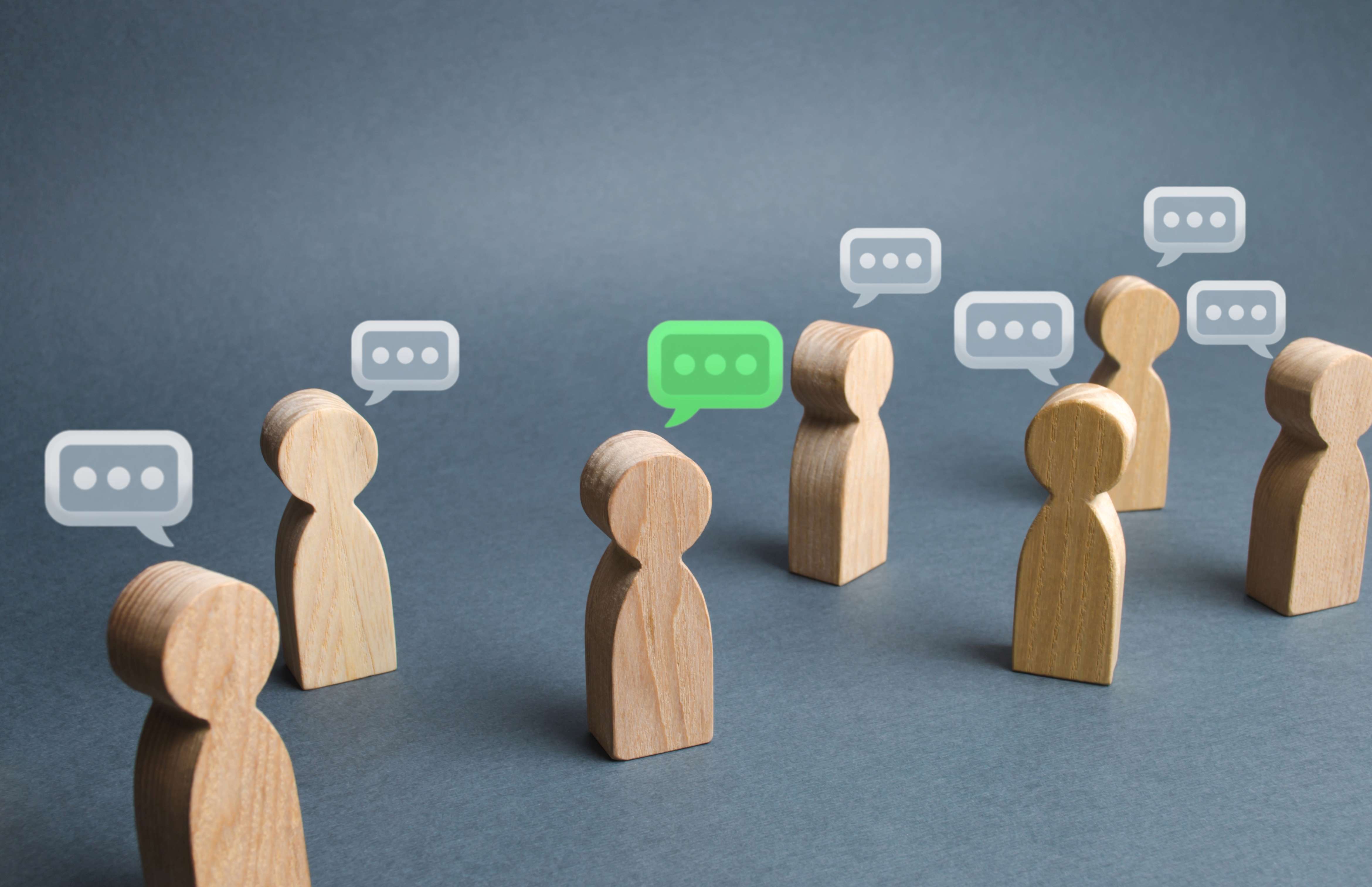 Little wooden people in a group with speech bubbles