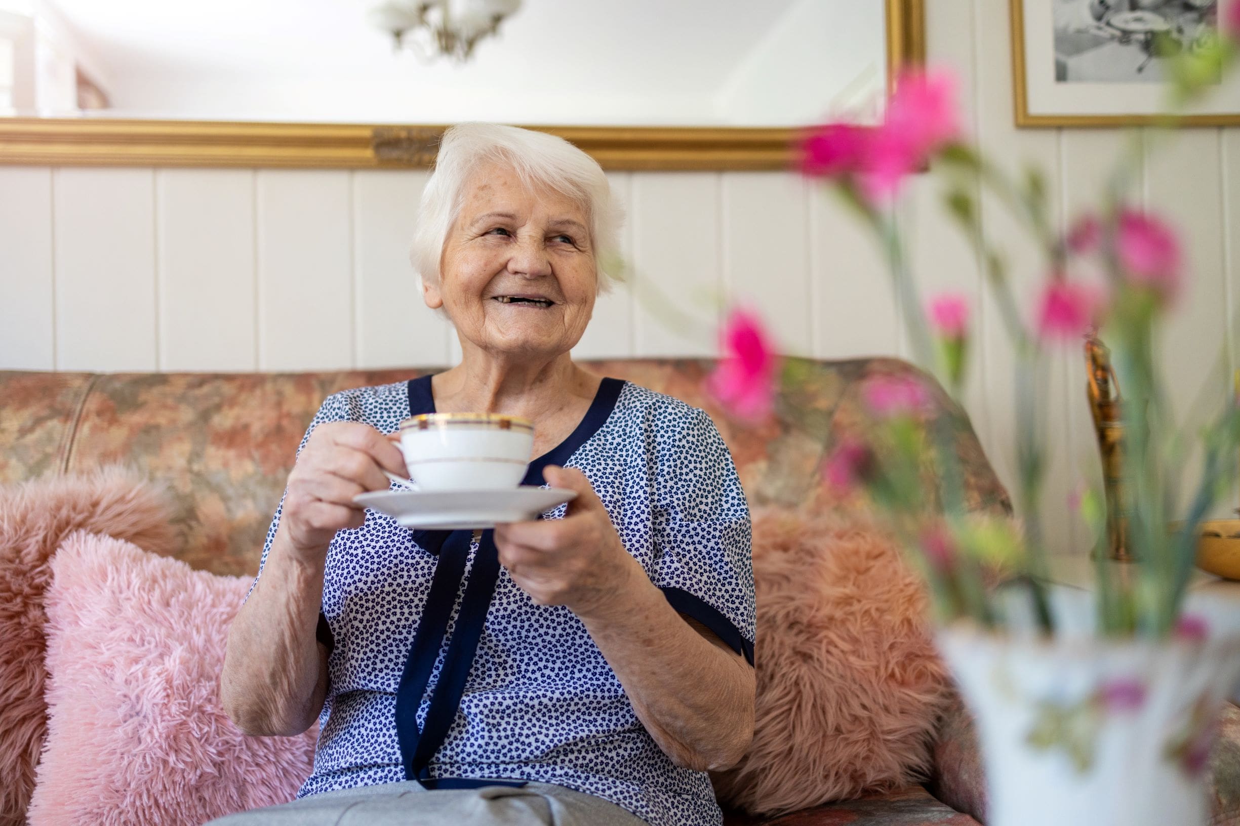 Older lady drinking tea sitting on a sofa and smiling