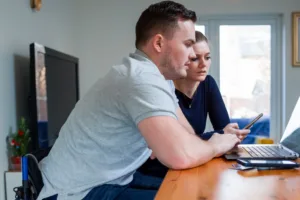two people looking at a laptop and a smart phone in their home