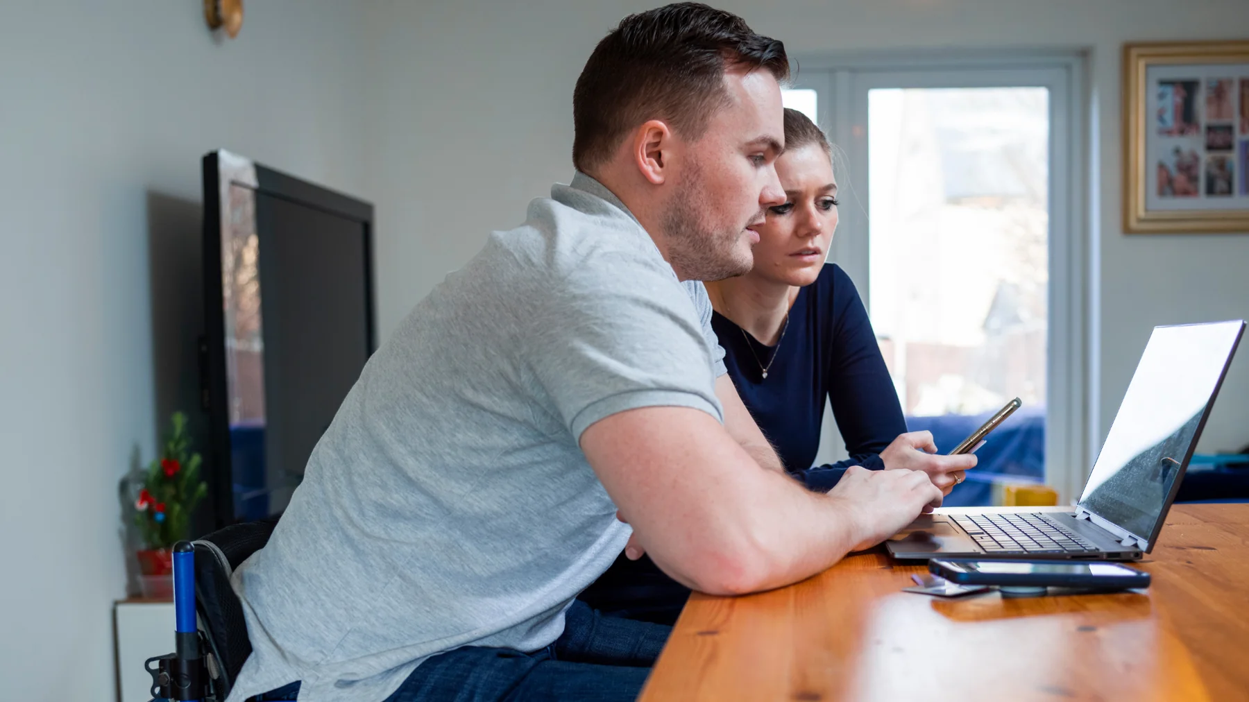 two people looking at a laptop and a smart phone in their home