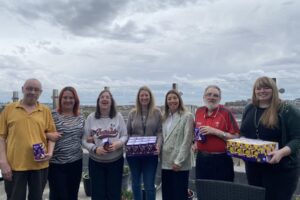 Seven people smiling and holding easter eggs against skyline backdrop