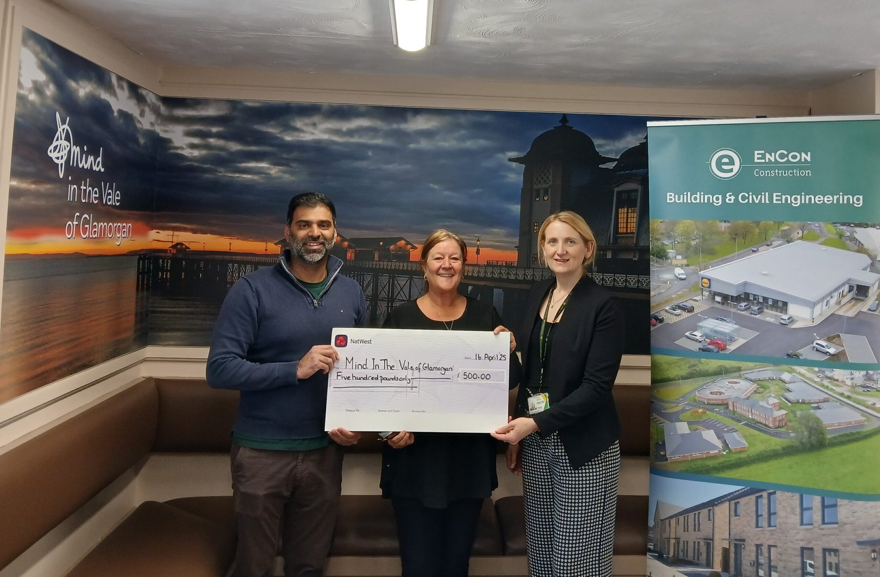 Three people smiling holding large cheque