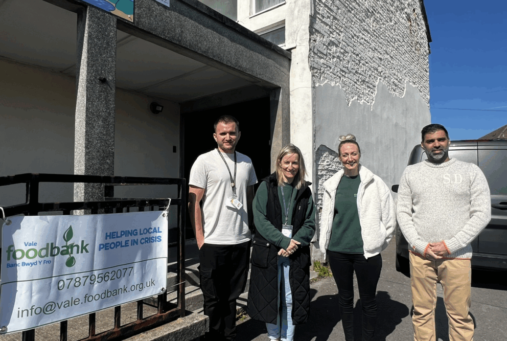 Four people smiling next to a banner that reads Vale Foodbank, Helping local people in crisis