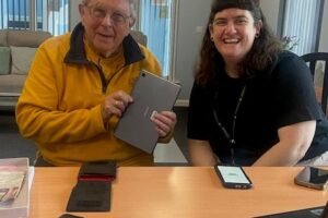 Two people sat at a table with laptop and phones
