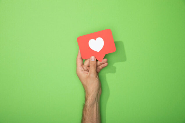cropped view of man holding red paper icon with white heart on green