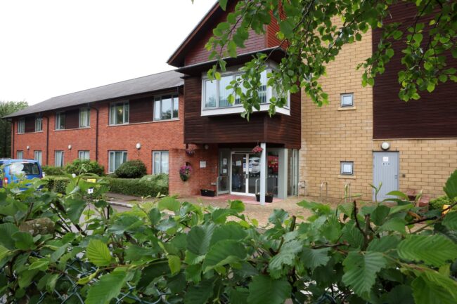 Exterior view of a residential building entrance, featuring mixed brickwork and wood cladding.