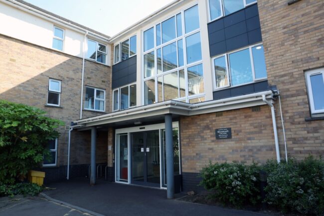 Woodcroft Care Home main entrance, featuring brickwork, glass doors, and large windows.