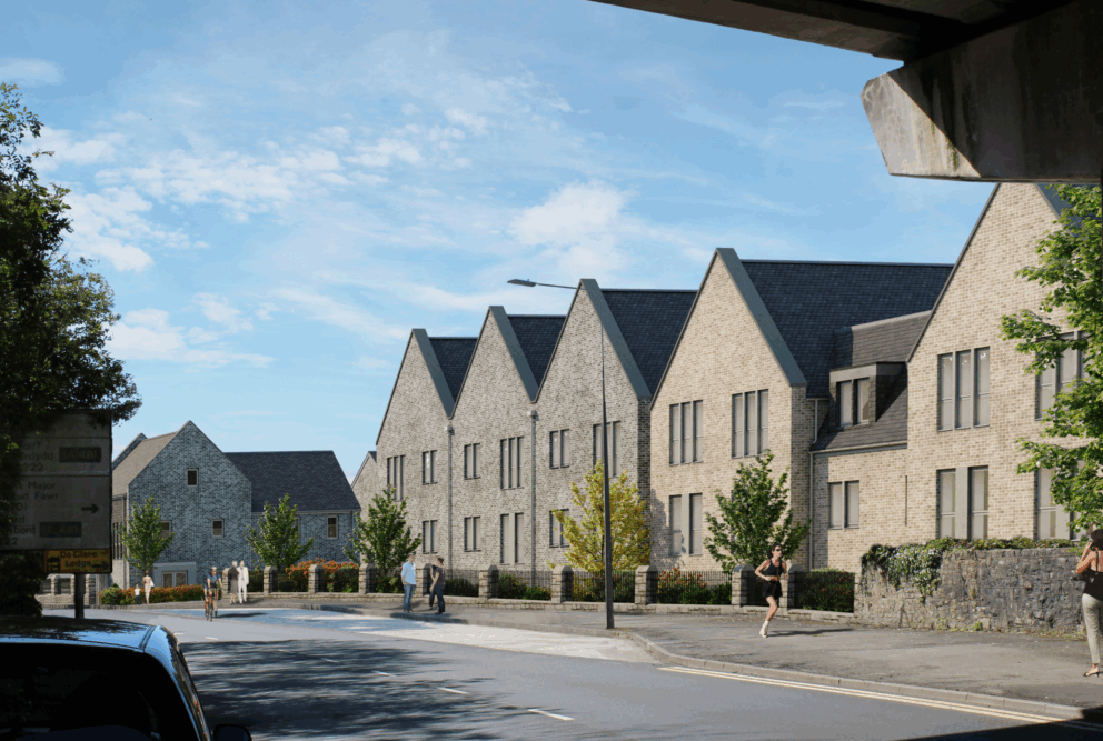Computer generated image of a row of modern stone buildings with pitched roofs along a street, with trees, a stone wall, and people walking under a clear blue sky