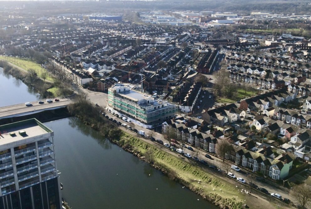 Aerial view of a large housing development under construction, wrapped in scaffolding and green netting.