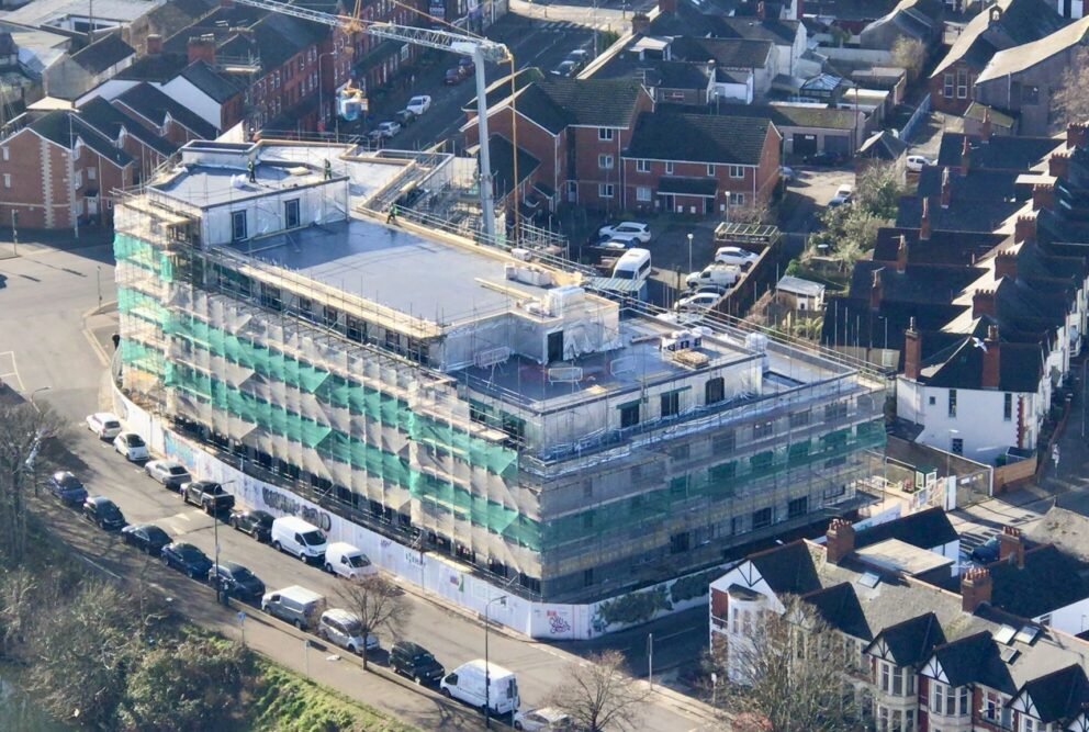Aerial view of a large housing development under construction, wrapped in scaffolding and green netting.