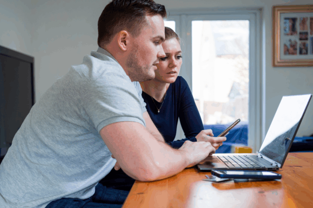 two people looking at a laptop and a smart phone in their home