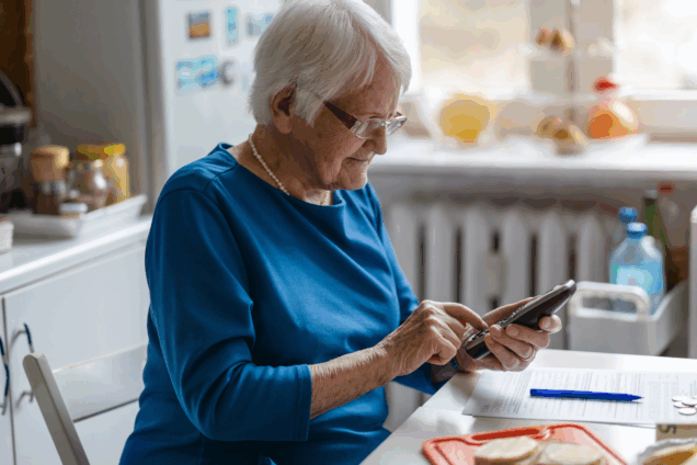 an older lady dialling a number on a phone in her kitchen