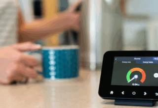 Close up of a smart meter and a blurry hand holding a cup in the background