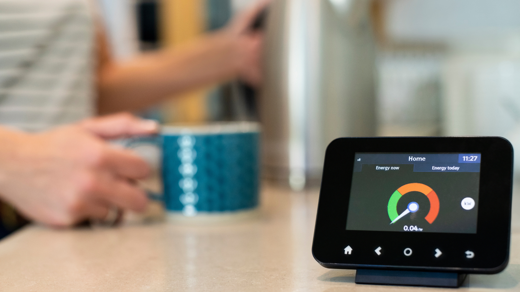 Close up of a smart meter and a blurry hand holding a cup in the background