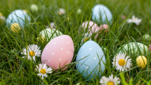 Eggs painted in pastel colours laying in a random order amongst the grass and daisies.