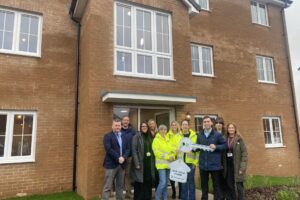 Group of people smiling, one holding a large key, stood in front of a new block of apartments