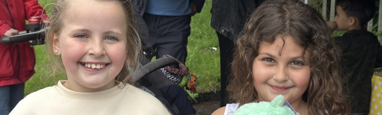 Two young girls similng to the camera, one on the right holds a cuddle toy