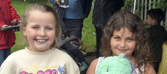 Two young girls similng to the camera, one on the right holds a cuddle toy