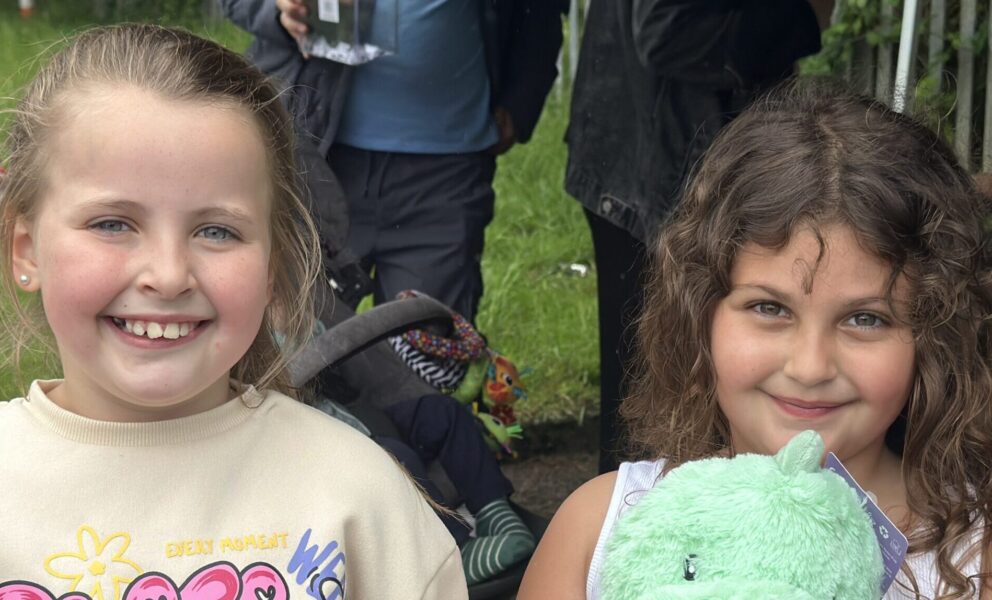Two young girls similng to the camera, one on the right holds a cuddle toy