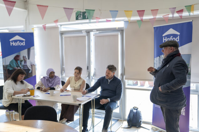 A group of people at a desk and one person standing up talking to them in a room