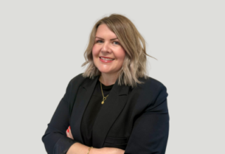 A lady with short blonde/brown hair folding her arms in a black jacket