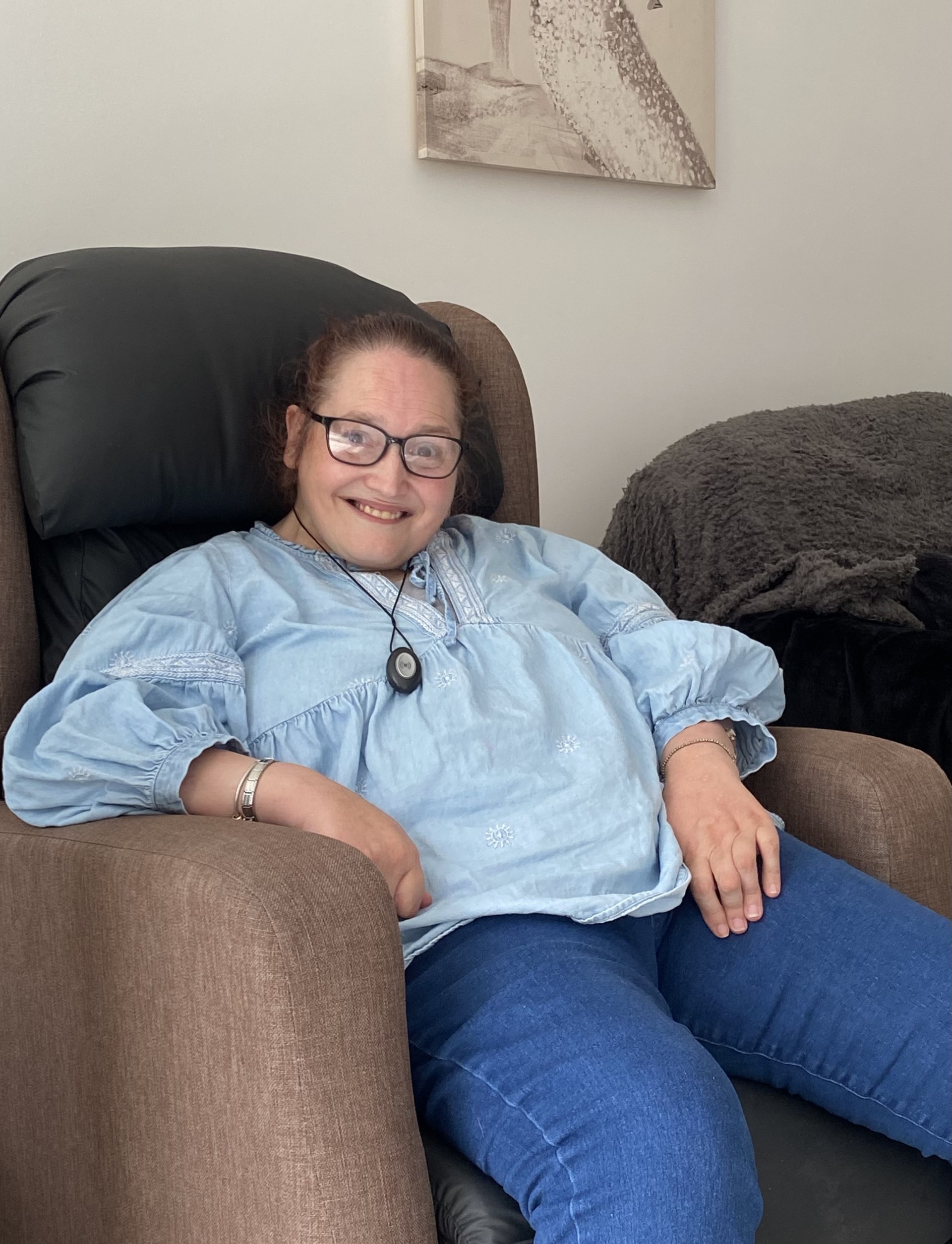 Photo of Stacey smiling, sat in her armchair at home