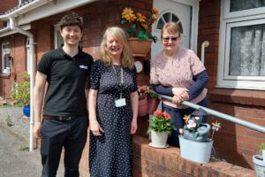 Three people smiling, stood outside front door of bungalow