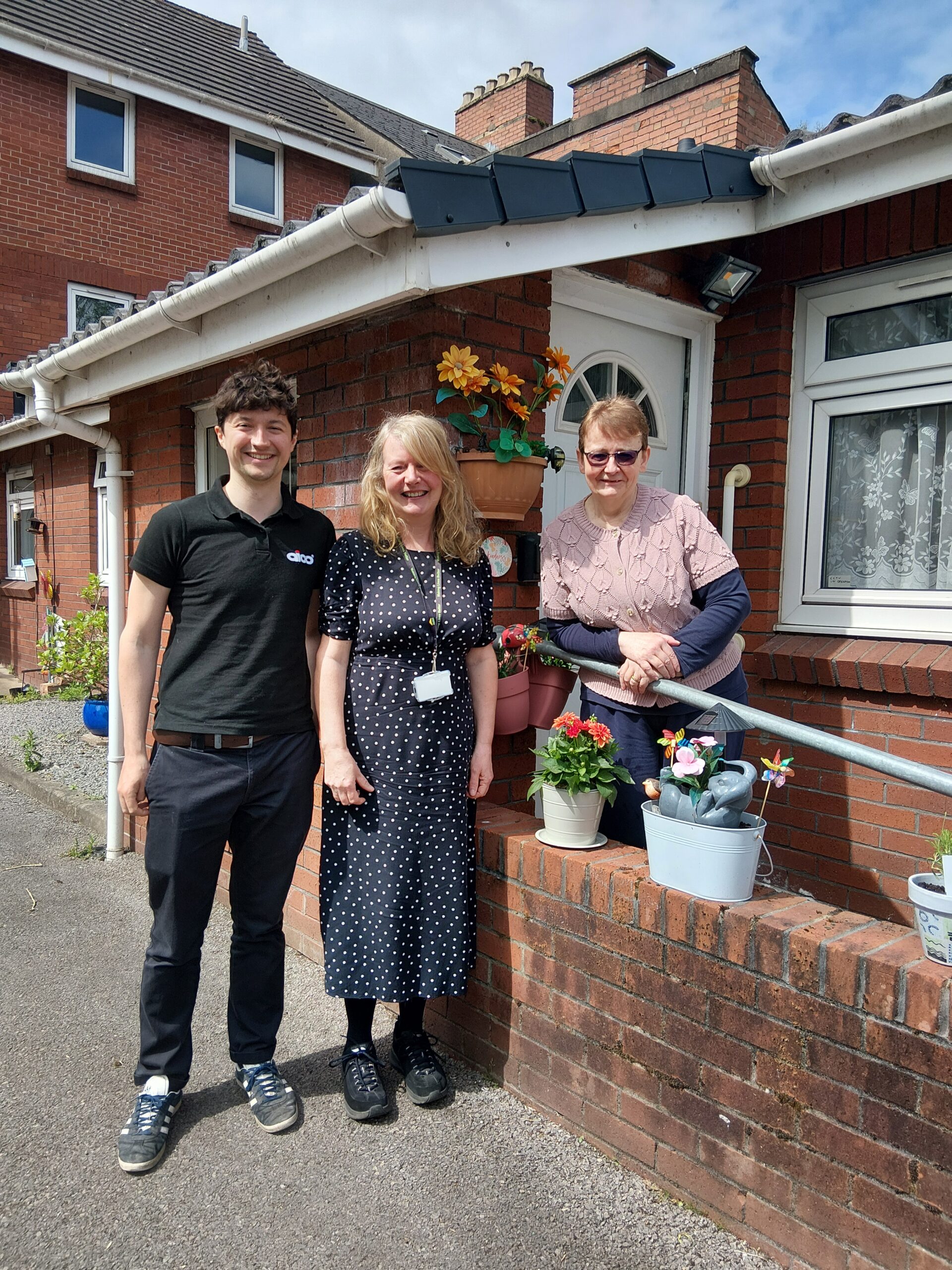 Three people smiling, stood outside front door of bungalow
